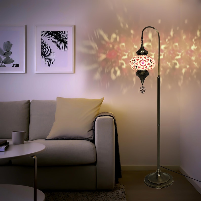 May include: A floor lamp with a white and pink mosaic glass shade. The shade has a geometric pattern and is accented with gold trim. The lamp has a curved arm and a gold base.