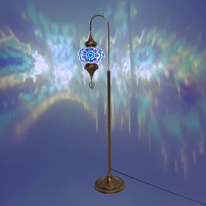 May include: A floor lamp with a blue and gold mosaic glass shade. The lamp has a curved arm and a round base. The shade casts a colorful pattern on the wall behind it.