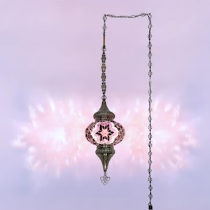 Op de afbeelding: Een decoratieve hanglamp met een mozaïek glazen kap in roze tinten en een sterontwerp. De lamp heeft een bronskleurig metalen frame en wordt opgehangen aan een ketting. De lamp is ontworpen voor gebruik binnenshuis.