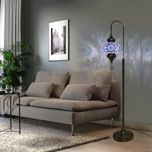 May include: A blue and white mosaic glass floor lamp with a curved arm and a decorative finial. The lamp is on a gray rug in a living room setting.