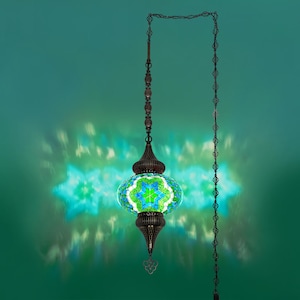 K&ouml;nnte beinhalten: Eine h&auml;ngende Mosaiklampe mit einem gr&uuml;nen und blauen Blumenmuster. Die Lampe hat einen dunklen Bronzemetallrahmen und eine Kette. Das Licht wirft ein sternf&ouml;rmiges Muster auf den gr&uuml;nen Hintergrund.