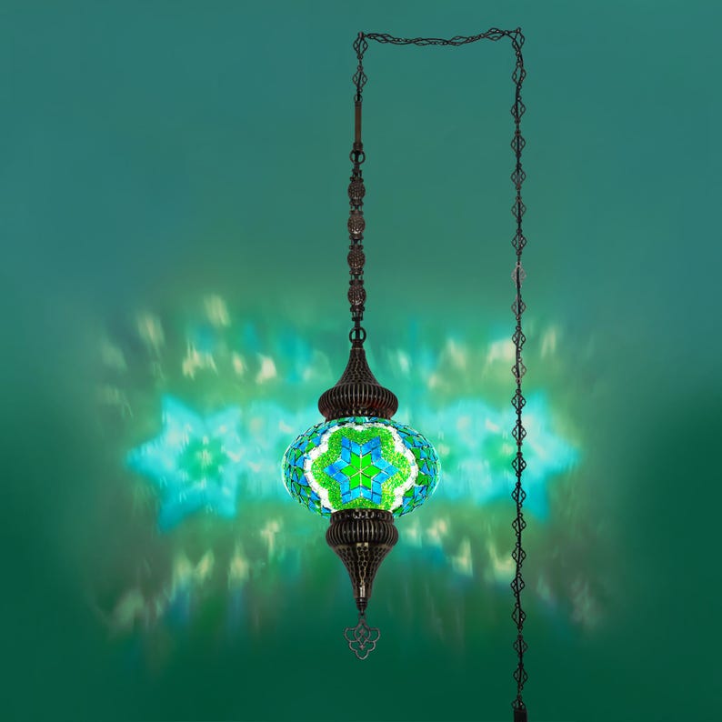 K&ouml;nnte beinhalten: Eine h&auml;ngende Mosaiklampe mit einem gr&uuml;nen und blauen Blumenmuster. Die Lampe hat einen dunklen Bronzemetallrahmen und eine Kette. Das Licht wirft ein sternf&ouml;rmiges Muster auf den gr&uuml;nen Hintergrund.