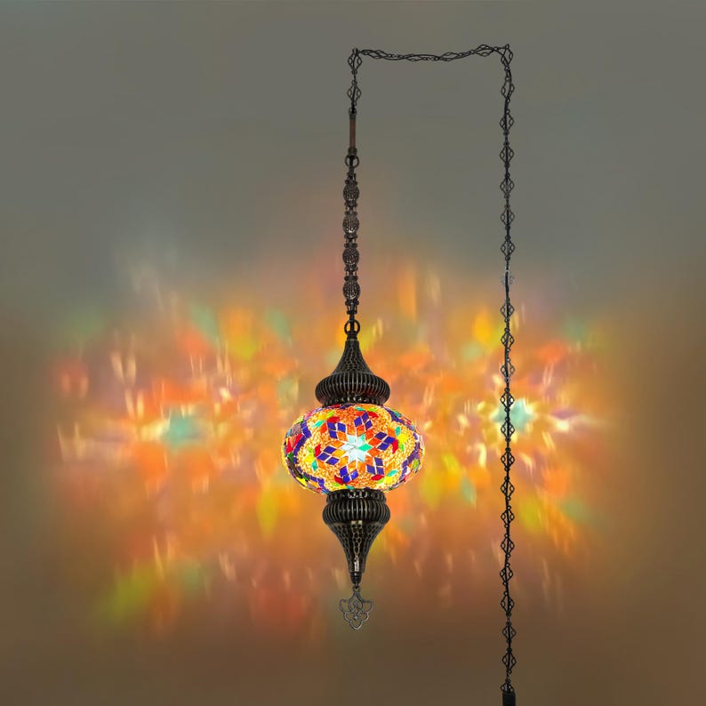 K&ouml;nnte beinhalten: Eine h&auml;ngende Mosaiklampe mit einer bunten, gemusterten Glaskugel. Die Lampe hat einen dunklen Metallrahmen und eine Kette und wirft ein lebendiges Licht auf die umgebende Oberfl&auml;che. Die Lampe ist an einer Kette aufgeh&auml;ngt.