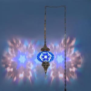 K&ouml;nnte beinhalten: Eine verzierte H&auml;ngelampe mit einem blau-wei&szlig;en Mosaikglasschirm. Die Lampe hat einen Metallrahmen und eine Kette, die ein sternf&ouml;rmiges Lichtmuster projizieren. Das Design der Lampe erinnert an t&uuml;rkische oder marokkanische Stile.