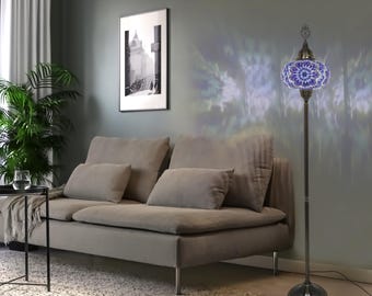 Peut inclure: Un lampadaire haut doté d'un abat-jour sphérique en verre avec un motif en mosaïque bleu et blanc. La lampe possède un pied en métal sombre et fin ainsi qu'une base circulaire, projetant une lumière à motifs sur le mur dans une pièce.