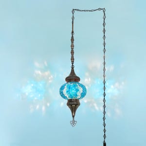K&ouml;nnte beinhalten: H&auml;ngeleuchte mit blau-wei&szlig;em Mosaikglasschirm. Die Lampe hat einen verzierten Metallrahmen und eine Kette, die vor einem hellblauen Hintergrund h&auml;ngt. Das Design ist von t&uuml;rkischen und marokkanischen Stilen inspiriert, mit einer Vintage-&Auml;sthetik.