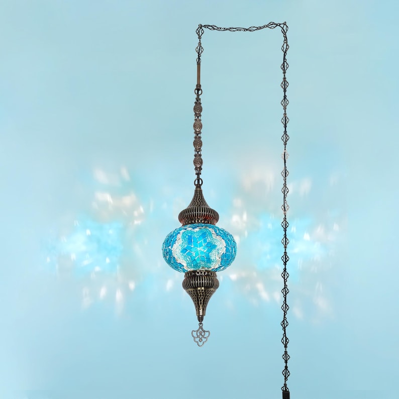 K&ouml;nnte beinhalten: H&auml;ngeleuchte mit blau-wei&szlig;em Mosaikglasschirm. Die Lampe hat einen verzierten Metallrahmen und eine Kette, die vor einem hellblauen Hintergrund h&auml;ngt. Das Design ist von t&uuml;rkischen und marokkanischen Stilen inspiriert, mit einer Vintage-&Auml;sthetik.
