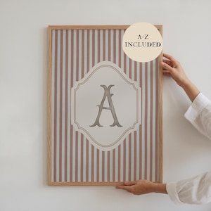 Op de afbeelding: Een ingelijste print met de letter "A" in een decoratief lettertype, tegen een crèmekleurige achtergrond met bruine en witte verticale strepen. De tekst "A-Z INCLUDED" staat in een cirkel rechtsboven.