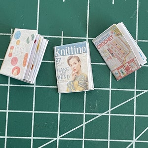 Puede incluir: Tres revistas en miniatura sobre una estera de corte verde. Las revistas se titulan "Knitting", "Creative Crochet" y "Libra Texts".