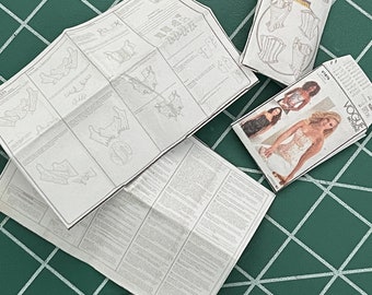 May include: A folded sewing pattern for a corset, a Vogue magazine featuring a model wearing a corset, and a folded sewing pattern for a corset from the company Butterick.