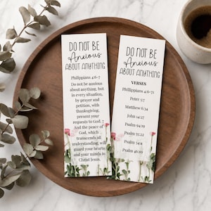 以下が含まれることがあります： 「DO NOT BE ANXIOUS ABOUT ANYTHING」のテキストと聖書の詩が書かれた2つの白いブックマーク。ブックマークの下部には花のアクセントがあり、コーヒーカップとユーカリの枝が入った木製のトレイの上にあります。