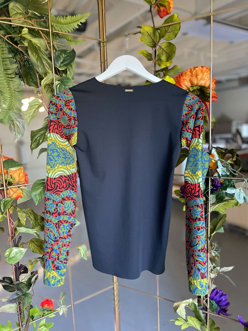 May include: Black long-sleeve shirt with colorful patterned sleeves. The sleeves feature a geometric design with red, green, blue, and yellow colors.