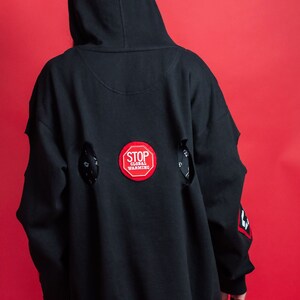May include: Black hooded sweatshirt with a red "STOP GLOBAL WARMING" patch on the back. The sweatshirt has distressed detailing with holes on the back.