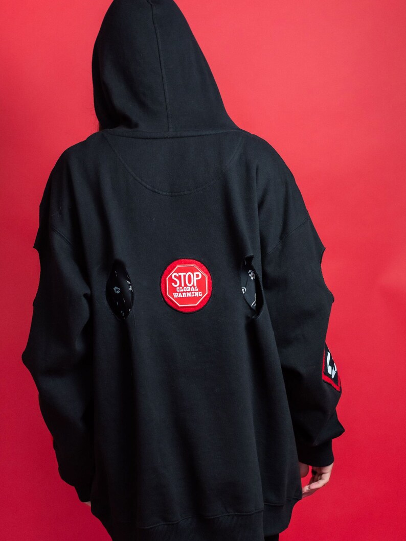 May include: Black hooded sweatshirt with a red "STOP GLOBAL WARMING" patch on the back. The sweatshirt has distressed detailing with holes on the back.
