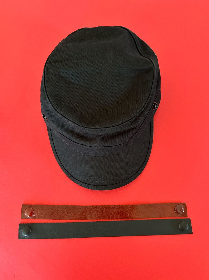 May include: A black canvas cap with a brown leather strap and a black leather strap with metal snaps.