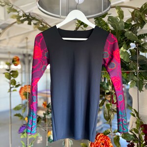 May include: A black long-sleeved dress with a square neckline and colorful floral print on the sleeves. The dress is hanging on a white hanger.