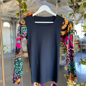 May include: A black long-sleeved shirt with a square neckline and floral print on the sleeves. The sleeves are a mix of pink, green, orange, and black.