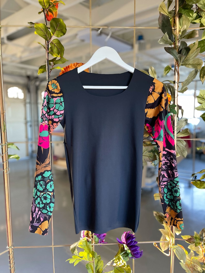 May include: A black long-sleeved shirt with a square neckline and floral print on the sleeves. The sleeves are a mix of pink, green, orange, and black.