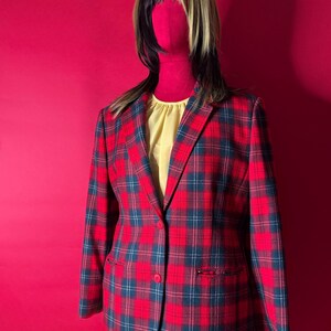 May include: A red plaid blazer with a single-button closure, featuring a classic tartan pattern in red, navy, and white. The blazer has two front pockets and is displayed on a mannequin with a yellow top and a two-tone wig.