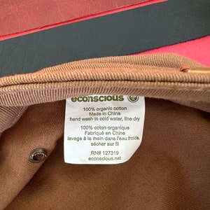 May include: A brown cotton cap with a white label that reads "econscious" and includes care instructions. The label says "100% organic cotton", "Made in China", "hand wash in cold water, line dry", "100% coton organique", "Fabriqu&eacute; en Chine", "lavage &agrave; la main dans l'eau froide, s&eacute;cher sur fil", "RN# 127319", and "econscious.net".