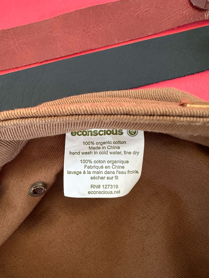 May include: A brown cotton cap with a white label that reads "econscious" and includes care instructions. The label says "100% organic cotton", "Made in China", "hand wash in cold water, line dry", "100% coton organique", "Fabriqu&eacute; en Chine", "lavage &agrave; la main dans l'eau froide, s&eacute;cher sur fil", "RN# 127319", and "econscious.net".