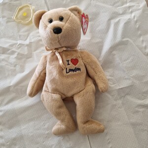 May include: A tan Beanie Baby plush bear with a red heart and the text "I Love London" on its chest. The bear has a brown nose and black eyes.