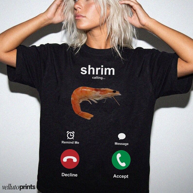 A woman wearing a black t-shirt with a graphic design depicting a shrimp and various icons representing different phone functions, such as a reminder, message, decline, and accept.