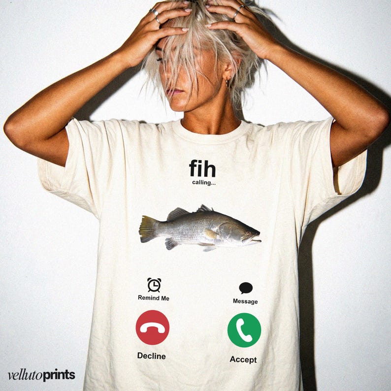 A person wearing a white t-shirt with a graphic design depicting a fish and various icons representing different forms of communication, such as a phone, a reminder, a message, and a decline.