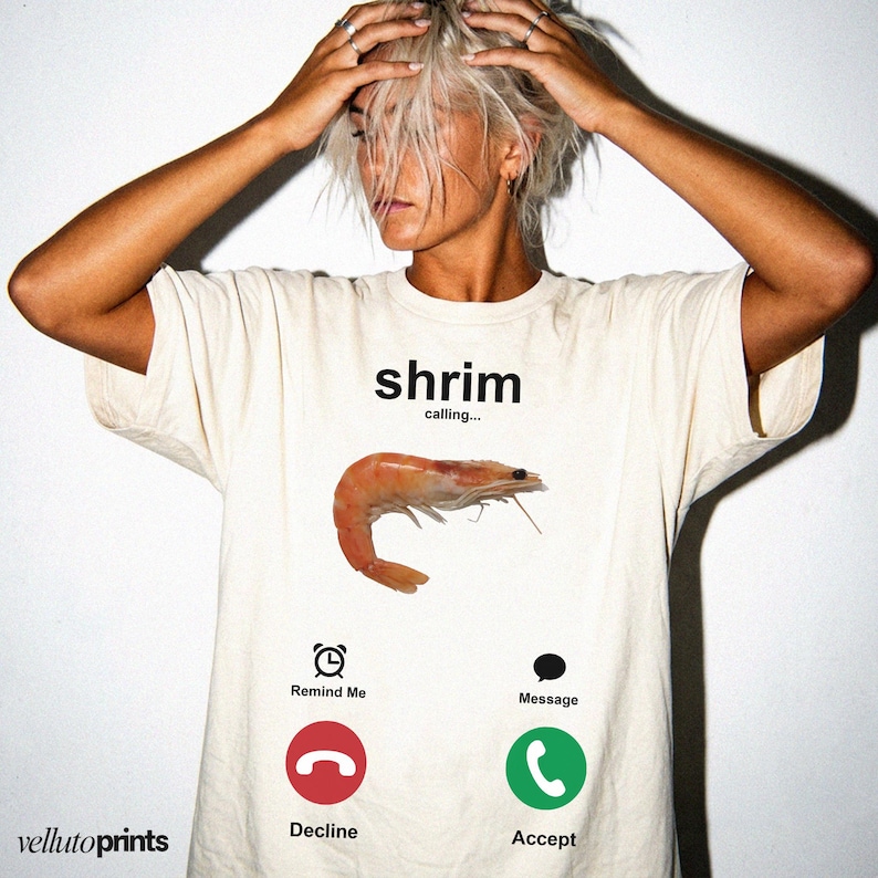 A person wearing a white t-shirt with a graphic design depicting a shrimp and various icons representing different types of communication, such as a phone call, a reminder, a message, and a decline or accept response.