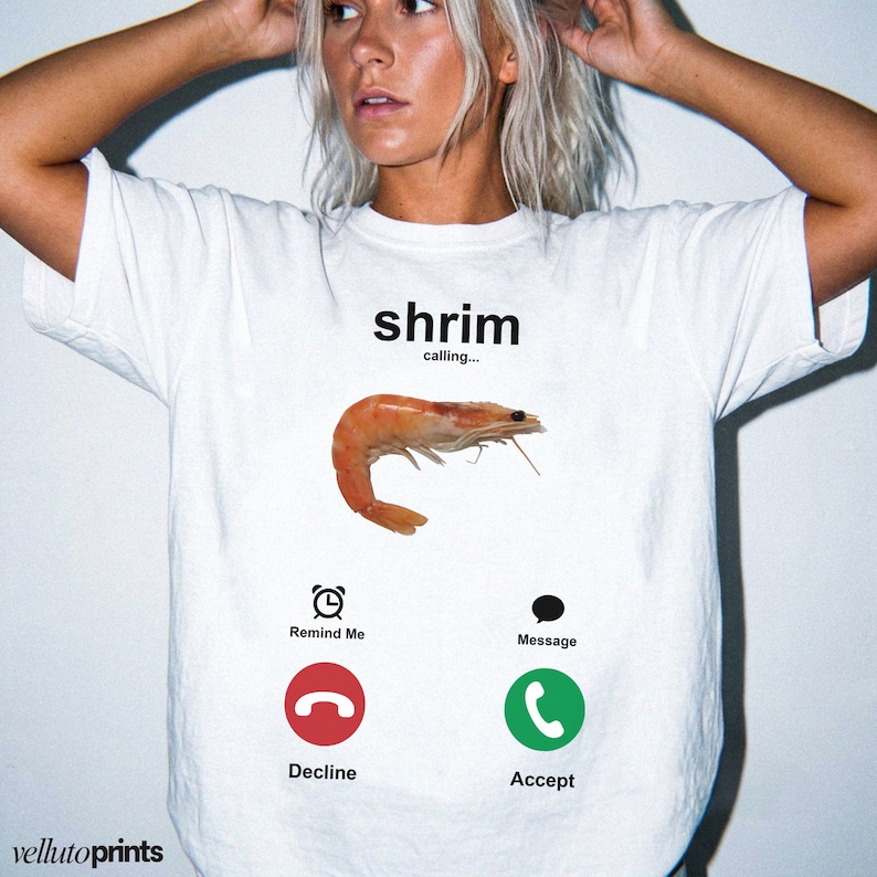 A woman wearing a white t-shirt with a graphic design depicting a shrimp and various icons representing different forms of communication, such as a phone call, a reminder, and a message.