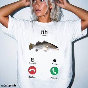 A woman wearing a white t-shirt with a graphic design depicting a fish and three icons representing a phone call, a message, and a decline.