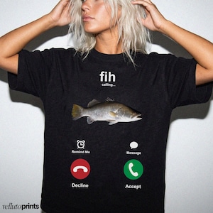 A woman wearing a black t-shirt with a graphic design depicting a fish and various icons representing different phone functions, such as a call, message, decline, and accept.