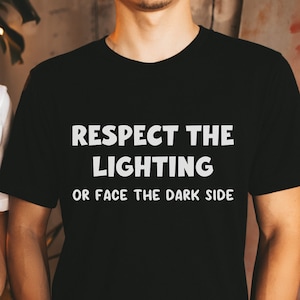 May include: Two people wearing black and white t-shirts with the text "Respect the Lighting or Face the Dark Side".