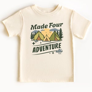May include: A cream colored t-shirt with a green and brown graphic of a sunset, mountains, and three tents. The text "Made Four Adventure" is printed in green on the shirt.