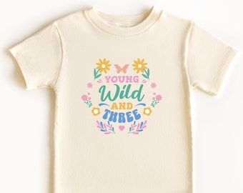 May include: A cream-colored t-shirt with a colorful graphic that says "Young Wild and Three" surrounded by flowers and butterflies.