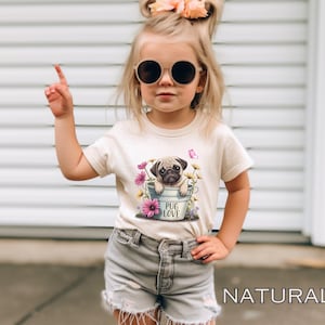 May include: A young girl wearing a light beige t-shirt with a graphic of a pug in a bucket with flowers and the text "Pug Love". She is wearing denim shorts and round sunglasses.