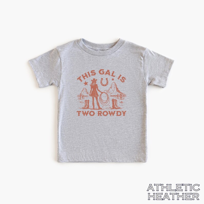 Puede incluir: Camiseta gris de manga corta con un gr&aacute;fico de una vaquera sosteniendo un lazo frente a una herradura y estrellas. El texto "This Gal Is Two Rowdy" est&aacute; impreso debajo del gr&aacute;fico.