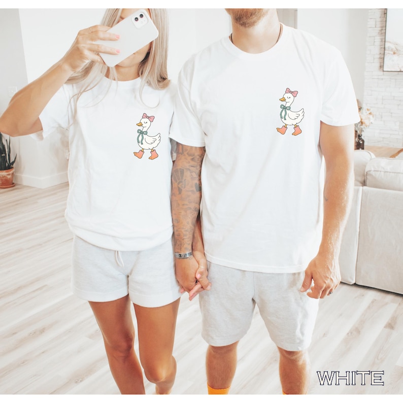 May include: White t-shirts with a cartoon goose design. The goose has a pink bow, green ribbon, and orange shoes. The shirts are paired with light gray shorts. The word "WHITE" is visible in the bottom right corner.