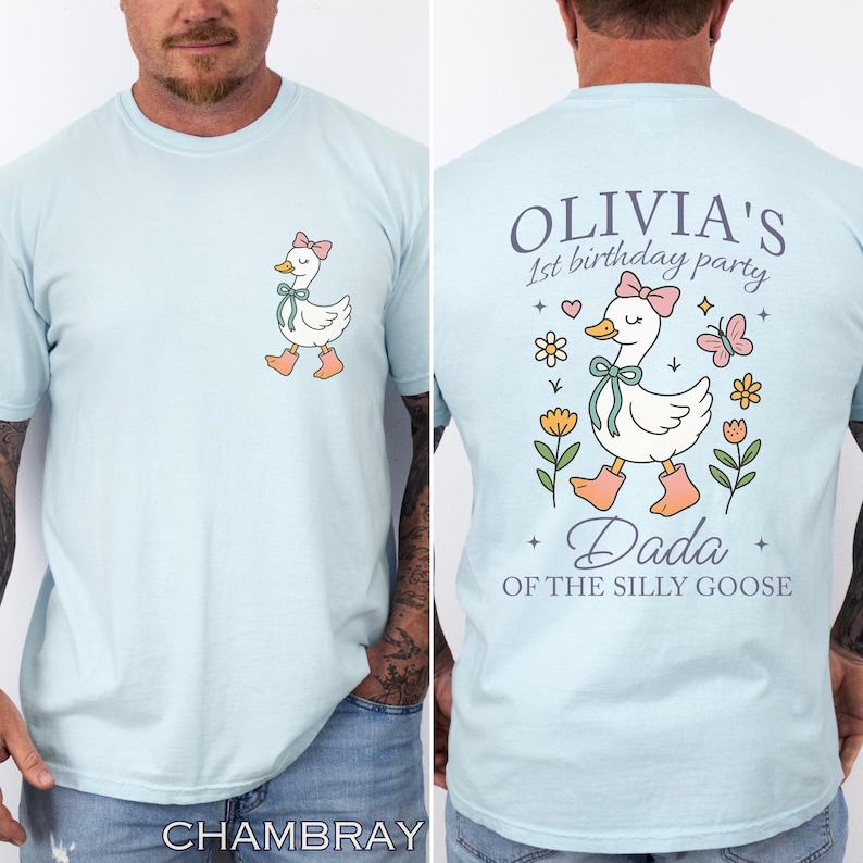 May include: Light blue t-shirt featuring a cartoon goose with a pink bow and boots. The back of the shirt has the text "Olivia's 1st birthday party" and "Dada of the silly goose" with floral and butterfly graphics.
