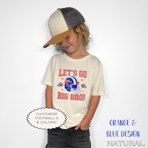 Puede incluir: Una camiseta color crema con el texto "LET'S GO BIG BRO!" en naranja y azul, con un gr&aacute;fico de casco de f&uacute;tbol americano. La camiseta se combina con una gorra de b&eacute;isbol con visera marr&oacute;n y parte superior de malla gris. Tambi&eacute;n se ve el texto "CUSTOMIZE FOOTBALL # & COLORS!".