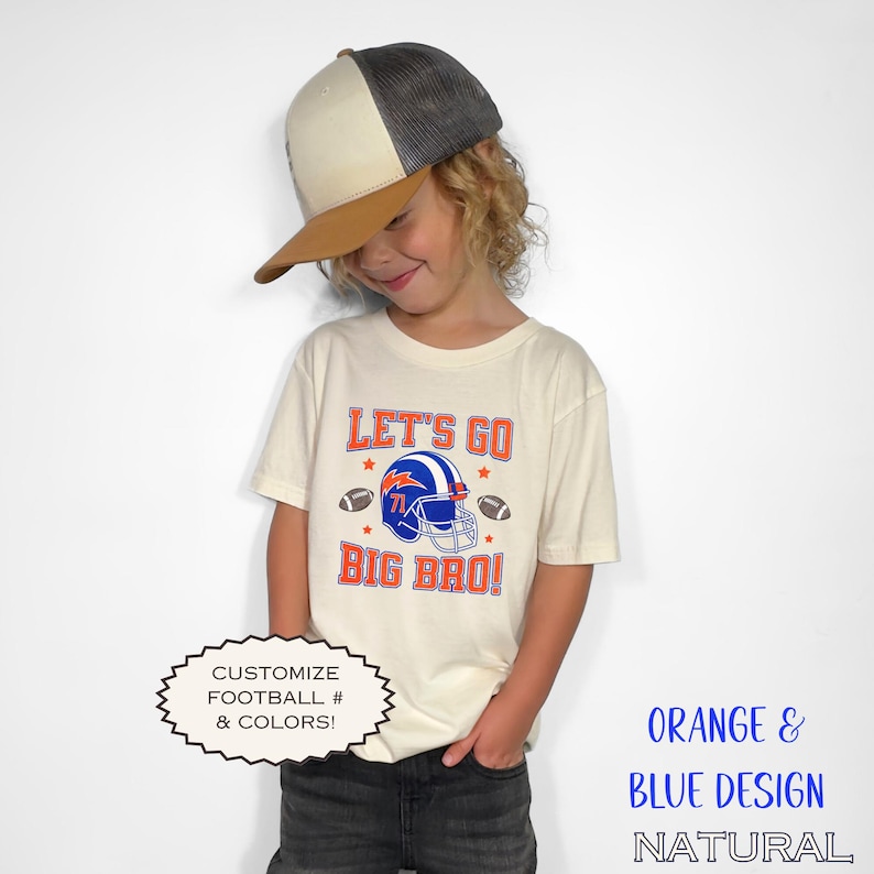 Puede incluir: Una camiseta color crema con el texto "LET'S GO BIG BRO!" en naranja y azul, con un gr&aacute;fico de casco de f&uacute;tbol americano. La camiseta se combina con una gorra de b&eacute;isbol con visera marr&oacute;n y parte superior de malla gris. Tambi&eacute;n se ve el texto "CUSTOMIZE FOOTBALL # & COLORS!".