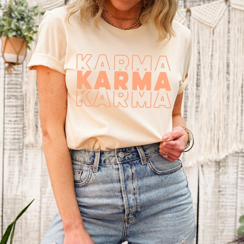 Może przedstawiać: Jasnobeżowy t-shirt z napisem "KARMA" powt&oacute;rzonym trzy razy w układzie piętrowym, w kolorze wyblakłego pomarańczowego.