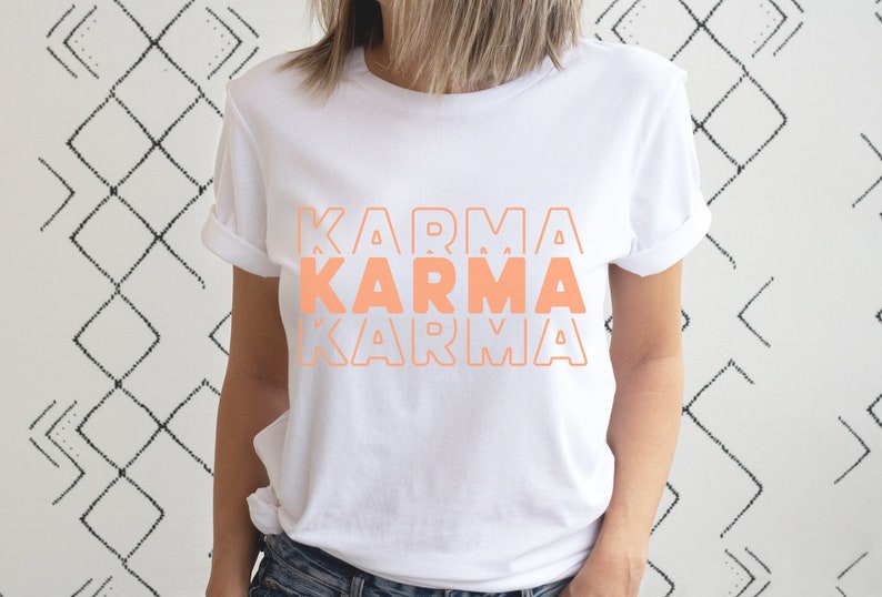Może przedstawiać: Biała koszulka z napisem "KARMA" powt&oacute;rzonym trzy razy w układzie piętrowym, w kolorze brzoskwiniowym.