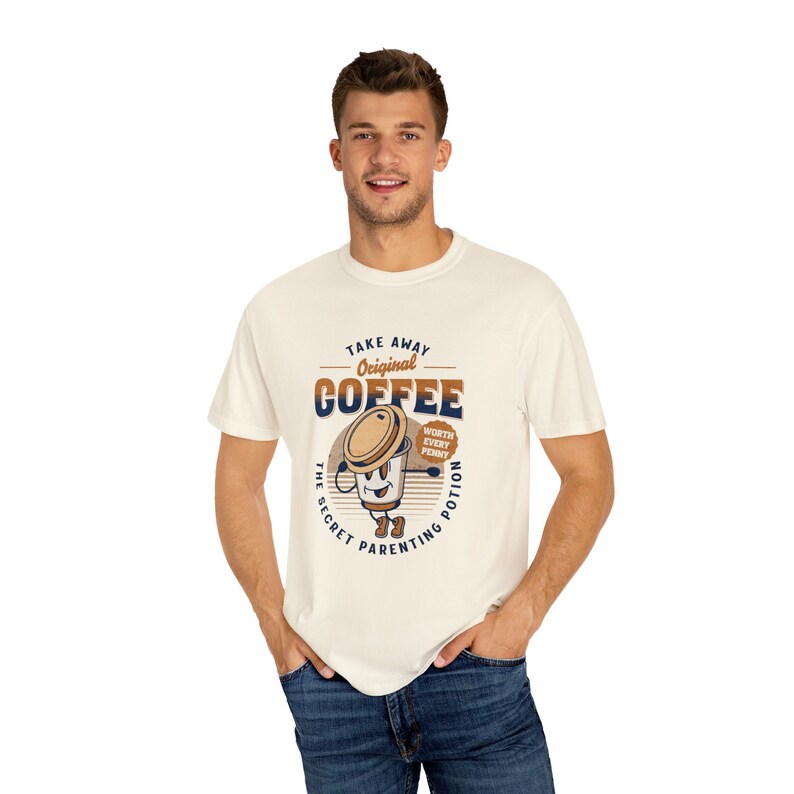 Op de afbeelding: Een wit T-shirt met een bruine en blauwe afbeelding van een koffiebeker met de tekst "Take Away Original Coffee The Secret Parenting Potion Worth Every Penny".
