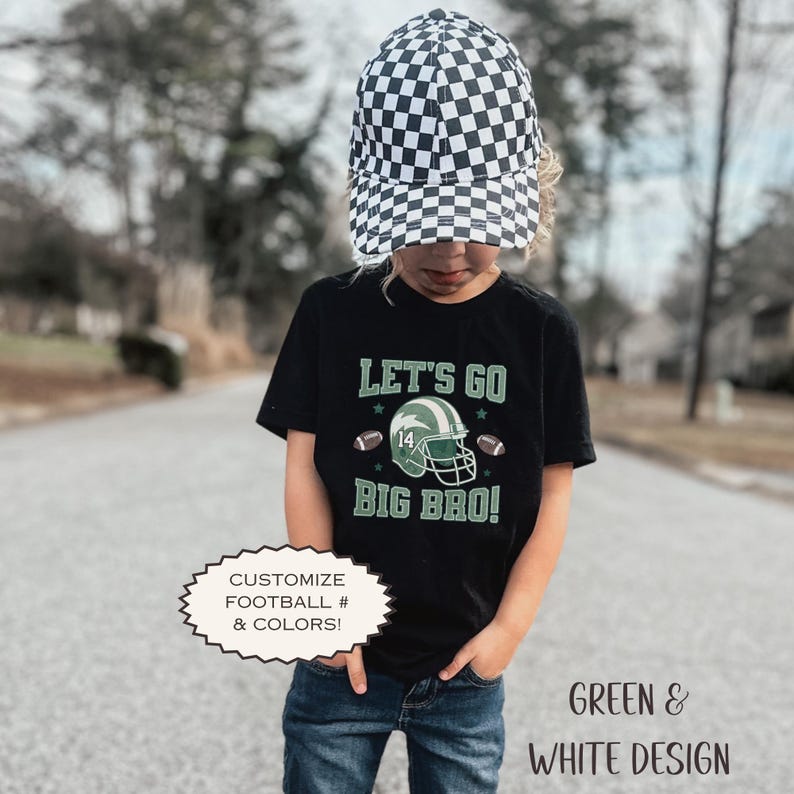 Puede incluir: Un ni&ntilde;o lleva una camiseta negra con el texto "LET'S GO BIG BRO!" y un gr&aacute;fico de casco de f&uacute;tbol. La camiseta tambi&eacute;n tiene dos balones de f&uacute;tbol y el n&uacute;mero 14. El ni&ntilde;o lleva un gorro a cuadros blanco y negro y vaqueros azules. Tambi&eacute;n se ve el texto "GREEN & WHITE DESIGN".