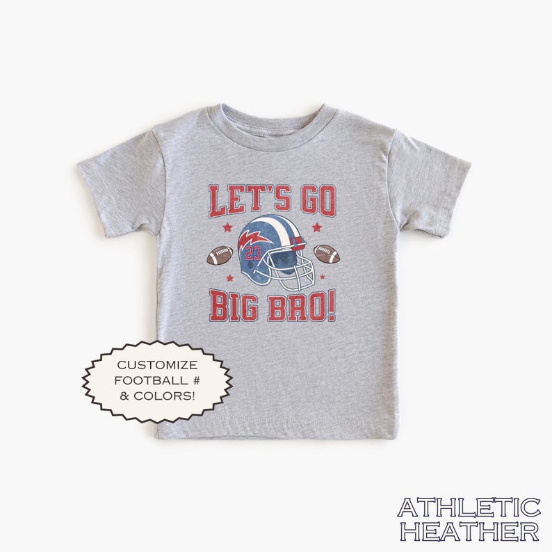 Puede incluir: Camiseta gris jaspeado de manga corta con un dise&ntilde;o de casco de f&uacute;tbol y el texto "LET'S GO BIG BRO!". El dise&ntilde;o incluye un casco azul y rojo, balones de f&uacute;tbol y estrellas. La camiseta tambi&eacute;n tiene el texto "PERSONALIZA F&Uacute;TBOL # & COLORES!"