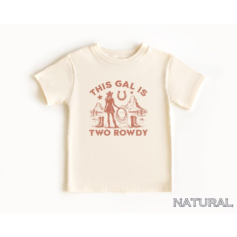 Puede incluir: Una camiseta de color crema con un gr&aacute;fico rojo de una vaquera con un lazo, una herradura y el texto "This Gal Is Two Rowdy".