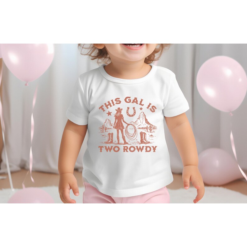 Puede incluir: Camiseta blanca con un gr&aacute;fico marr&oacute;n de una ni&ntilde;a con un sombrero de vaquero sosteniendo un lazo. El texto "This gal is two rowdy" est&aacute; impreso debajo del gr&aacute;fico.