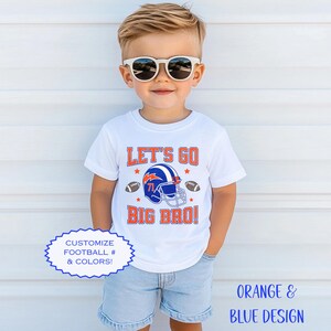 Puede incluir: Camiseta blanca con el texto "LET'S GO BIG BRO!" en naranja y un gr&aacute;fico de casco de f&uacute;tbol azul. La camiseta tambi&eacute;n presenta dos balones de f&uacute;tbol y estrellas. El dise&ntilde;o es personalizable con n&uacute;meros y colores de f&uacute;tbol.