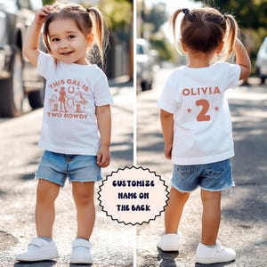 Puede incluir: Camiseta blanca con un gr&aacute;fico rosa que dice "This gal is two rowdy" y una silueta de vaquera. La parte posterior de la camiseta tiene una estrella rosa a cada lado del n&uacute;mero 2 y el nombre "Olivia" en rosa.